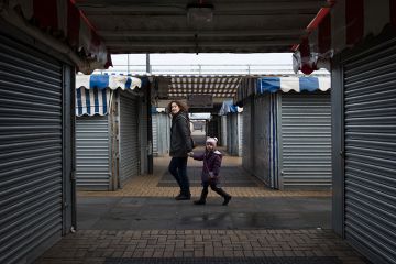 A woman and child walk through a market area with closed stalls in Milton Keynes, England.