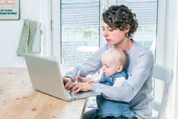 Mother working on laptop in kitchen with baby Mother working on laptop in kitchen with baby