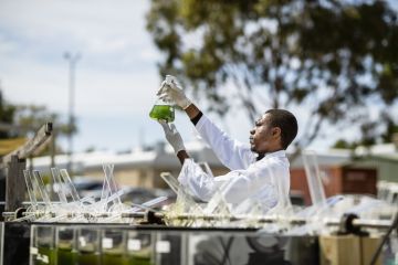 A young scientist working on research outdoors, holding up a glass beaker and inspecting the liquid inside, symbolising open science 