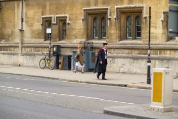Oxford United Kingdom - June 19 2009; University city street scene with man in gown and mortarboard or Oxford cap walking on sidewalk.