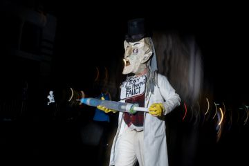 Parader dressed as Dr. Fauci holds a giant syringe protesting vaccines at the annual 6th Ave Halloween Parade in NYC