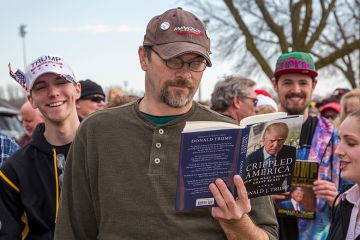A man reads a Donald Trump book while waiting in a long line for admission to a Trump campaign rally, 2016. To illustrate that academics might need to 'tread carefully' with courses on Trump.