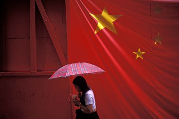 A large banner Chinese flag hangs over a pedestrian under an umbrella. To illustrate that there is ‘little universities can do’ to stop Beijing interference.