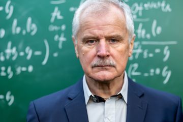 A glum old professor in front of a blackboard