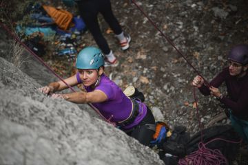 One rock climber hold the rope for another, illustrating a supportive research environment