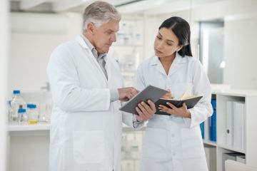 A senior scientist shows a junior scientist something on a tablet A senior scientist shows a junior scientist something on a tablet