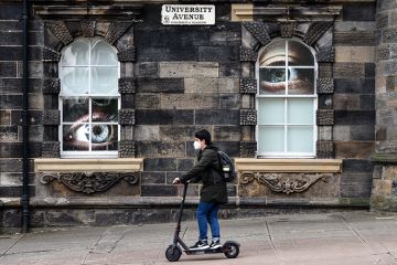 Student on a scooter on campus at the University of Glasgow, with large eyes looking at him through windows. To illustrate the university being placed on a student visa sponsorship “action plan” by the Home Office Student on a scooter on campus at the University of Glasgow, with large eyes looking at him through windows. To illustrate the university being placed on a student visa sponsorship “action plan” by the Home Office