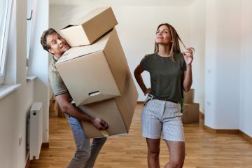 A man carries heavy boxes while a woman looks on