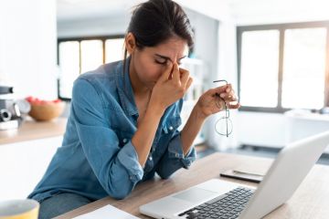stressed woman working from home on laptop looking worried, tired and overwhelmed