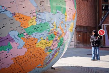 A student holds a Help paddle for those wanting advice during an open-day for prospective students alongside a sculpture of the world, London School of Economics, 9 April 2025. To illustrate international students.