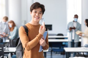 student removing disposable surgical face mask, standing at classroom