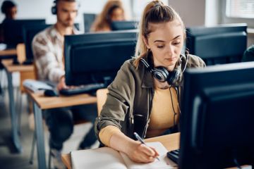 A university student writes notes while e-learning on a computer in the classroom A university student writes notes while e-learning on a computer in the classroom