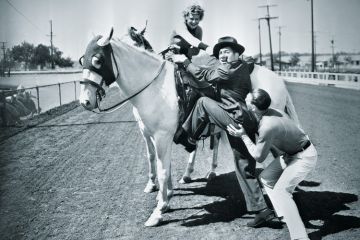 Young couple trying to help a man get onto his horse