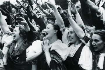 Ethnic Germans wearing traditional regional costumes give the Nazi salute and cheer Adolf Hitler on his visit to the town of Carlsbad in the Sudetenland
