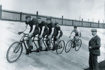 A four-man cycling tandem team in training with the 'chase and pacemaker' whilst being timed on the stopwatch.