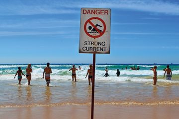 People in the sea at Manly beach, Australia with "dangerous currents" sign.