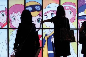 People silhouetted against a screen showing Japanese anime People silhouetted against a screen showing Japanese anime