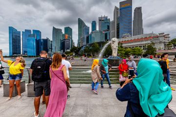 Tourists of various nationalities pose for photos in front of the Merlion statue and Singapore skyline, illustrating Singapore’s international nature Tourists of various nationalities pose for photos in front of the Merlion statue and Singapore skyline, illustrating Singapore’s international nature