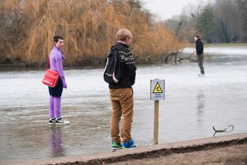 Frozen lake with sign for Danger Thin Ice with people standing on it, as an illustration of the ‘wafer-thin margins’ faced by middle-tier universities as financial challenges arise from government proposal for a overseas student levy.