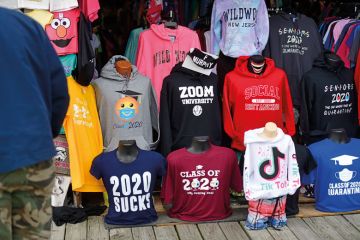  Tourists shop for boardwalk t-shirts including "ZOOM UNIVERSITY," "SOCIAL DISTANCING," and "2020 SUCKS" to illustrate Leading US universities settle Covid online teaching lawsuits