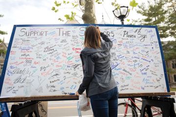  A woman signs a board in support of survivors of sexual abuse at a vigil in front of the home of outgoing University of Michigan President Mark Schlissel to illustrate the story 