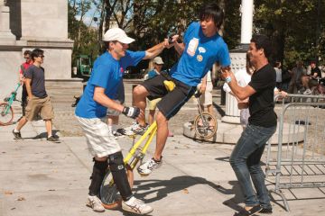 Unicyclist stumbles with two people supporting him to illustrate uncertainty on wait lists as US colleges face enrolment disruption