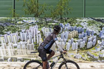 A cyclist rides past an artist illustration of buildings at a construction site in the Kwu Tung area in Hong Kong, China A cyclist rides past an artist illustration of buildings at a construction site in the Kwu Tung area in Hong Kong, China to illustrate ‘University town’ will give Hong Kong campuses room to grow
