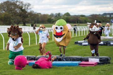 Runners dressed as mascots with a  dinosaur fallen in front to illustrate 