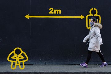 Woman walks by 2metres apart sign with diagram of person sitting down as a metaphor for Will Covid reset  the help given to deprived students.