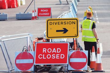 Worker standing with road-signs as a metaphor for shortages at labs caused by border snarls and new rules.