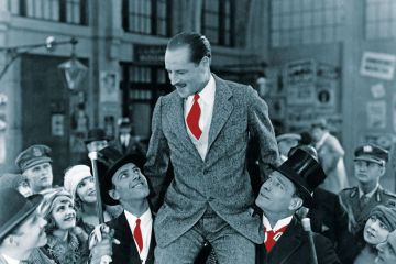 Man carried on shoulders above crowd to illustrate Who’s a jolly good fellow?