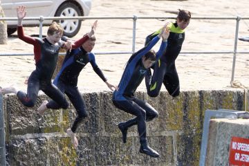 Four people jumping off from a harbour wall as a metaphor for cutting English fees and student numbers.