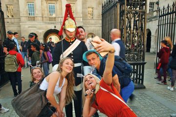 King's guard stands to attention guarding the entrance to the Horse Parade while tourists take a selfie King's guard stands to attention guarding the entrance to the Horse Parade while tourists take a selfie to illustrate Age of the influencer?