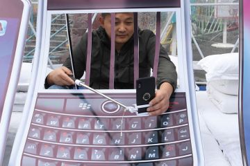 Person with arms behind art installation bars holding his mobile phone other side of bars