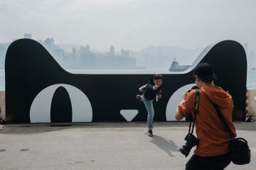 A man poses for a photograph in front of a billboard featuring the Tmall Cat, mascot for Alibaba Group Holding Ltd.'s Tmall online marketplace to illustrate Alibaba makes inroads in Europe