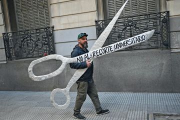 A demonstrator holds a giant scissors that read in Spanish "No to the University Cuts" to illustrate Argentine academics flee Milei’s austerity crusade