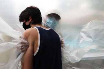 John Sileo hugs his grandfather, Domenik Sileo through a plastic drop cloth hung up on a homemade clothes line during Memorial Day Weekend on May 24, 2020 in Wantagh, New York.