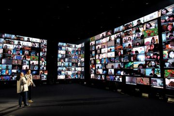 People on screens two people standing laughing.