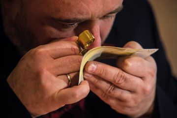 An employee examines with magnifier glass counterfeit 200 Euro bank note to illustrate Problems with bank checks drive student visa refusals