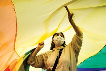 Person standing under an LGBT flag as a metaphor for Melbourne revises free speech rules over transgender concerns.