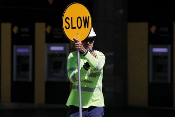 A traffic control worker holds a traffic sign reading "Slow" in Brisbane, Australia to illustrate Visa chaos ‘latest driver’ of ‘two-tiered Australian sector’