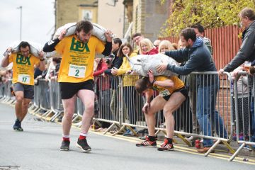 Competitors in a coal carrying race with large heavy sack on their back and one man from a crowd helping a sack on a competitors back as a metaphor  to Crowdfunding is increasingly a way for scholars and students at less prestigious universities to gain r