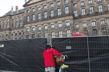 A woman peeks through the fence at the Royal Palace, Netherlands to illustrate Amsterdam ‘experiment’ with language caps ‘legally risky’