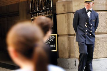 A doorman works in front of a landmark building to illustrate More US states to automatically enrol high schools’ top graduates in college