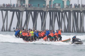 Crowds gather on the pier and the beach to watch surfing break the World Guinness Record for most people (66) on a surfboard and the biggest surf board (42 1/4 feet) in Huntington Beach, California to illustrate Biden officials open to more three-year deg