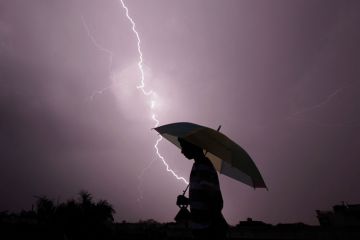 A pedestrian walks with an umbrella as lightning strikes to illustrate Pressure on Ashoka builds as intelligence services visit campus