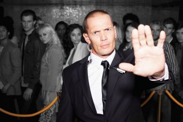 Bouncer with arm outstretched outside nightclub