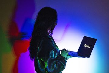 A woman looks at a laptop screen displaying the logo of 'OpenAI', to illustrate that academics question the pedagogical impact of AI learning assistants.