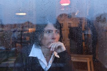 A woman looks out of a rain-splashed window, illustrating genderwashing A woman looks out of a rain-splashed window, illustrating genderwashing