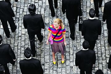 Young woman in a crowd of people in black suits illustrating feature article about US undergraduate university system